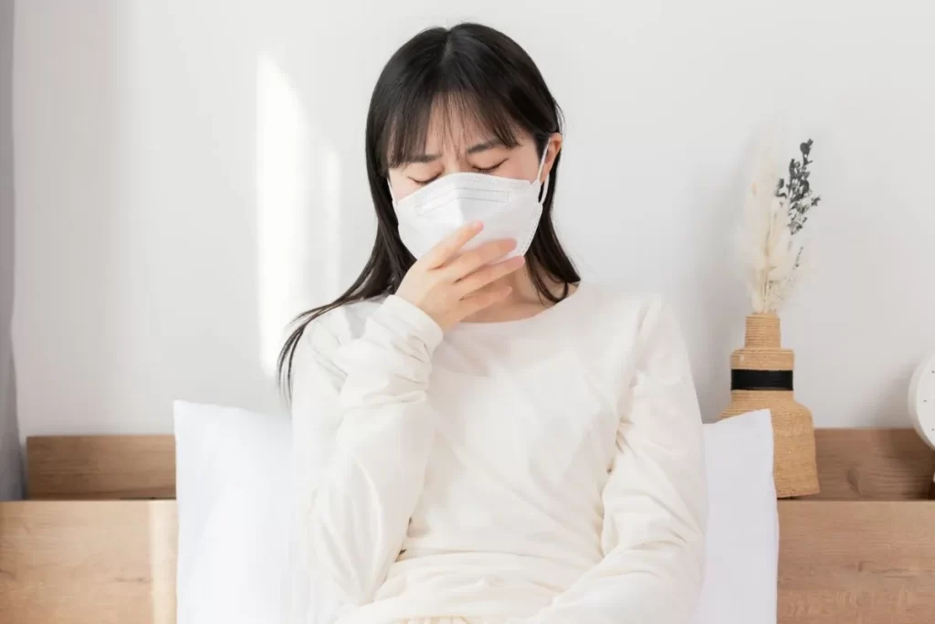 花粉症でつらそうな40代女性。マスクをして目を閉じ、口元を手で押さえている様子。