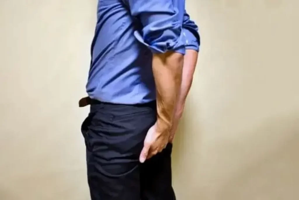 痔の不快感で肛門あたりを両手で押さえる青いシャツの男性