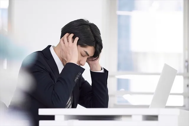 デスクで肘をつき頭を抱える悩み疲れたビジネスマン。考えすぎによるストレスを表現