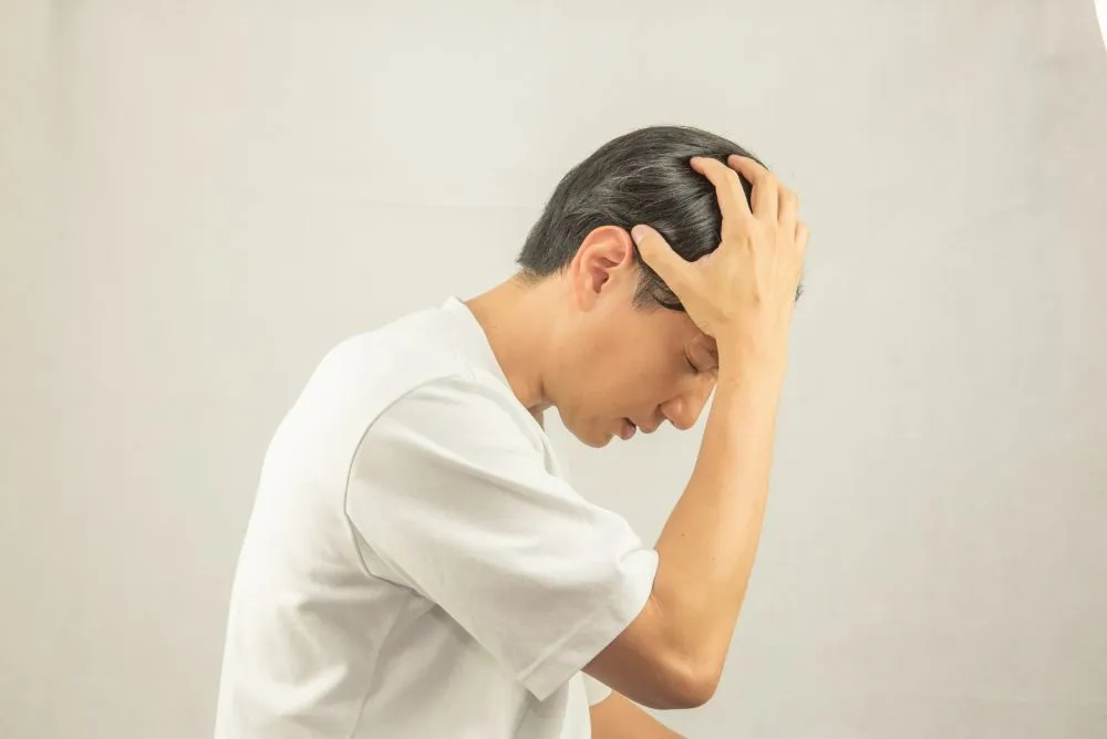 めまいを感じて頭を押さえる男性の鍼灸治療後の好転反応