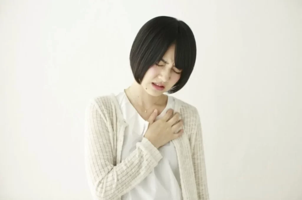 白い服を着た女性が左胸を抑え、胸の苦しさや不整脈を表現しているイメージ