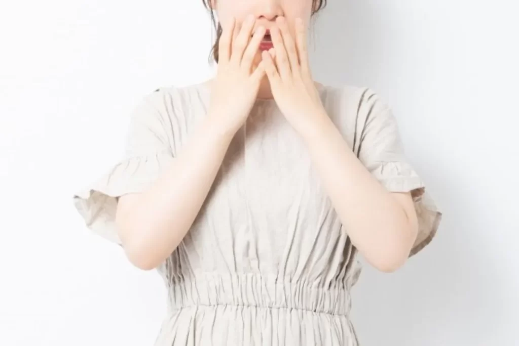 突然の衝撃的な事件で驚き、両手で口を覆う女性。生理が来なくなったきっかけとなるショックの様子を表しています。