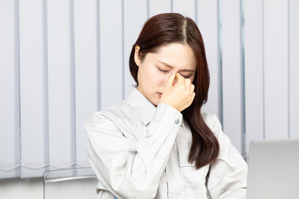 白い工作服を着た女性が、目の疲れや複視の不快感から目の内側を押している様子