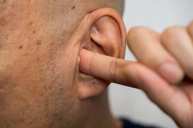 耳鳴り（セミの音）を気にする男性が耳に人差し指を入れる様子
