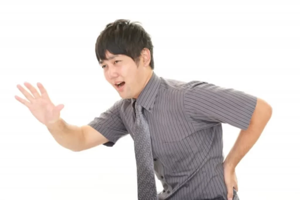 腰痛で苦しむ男性が左手で腰を押さえ、助けを求めるように右手を伸ばしている様子