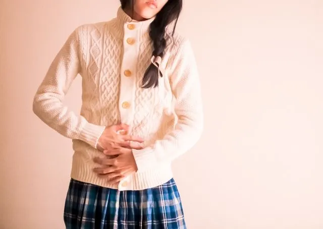 生理痛でお腹を抱える白いセーターの女性。眼精疲労や生理痛のつらい症状を鍼治療で即解消