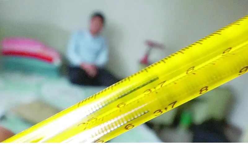 高熱でぐったりした人を背景に黄色い温度計をクローズアップした画像