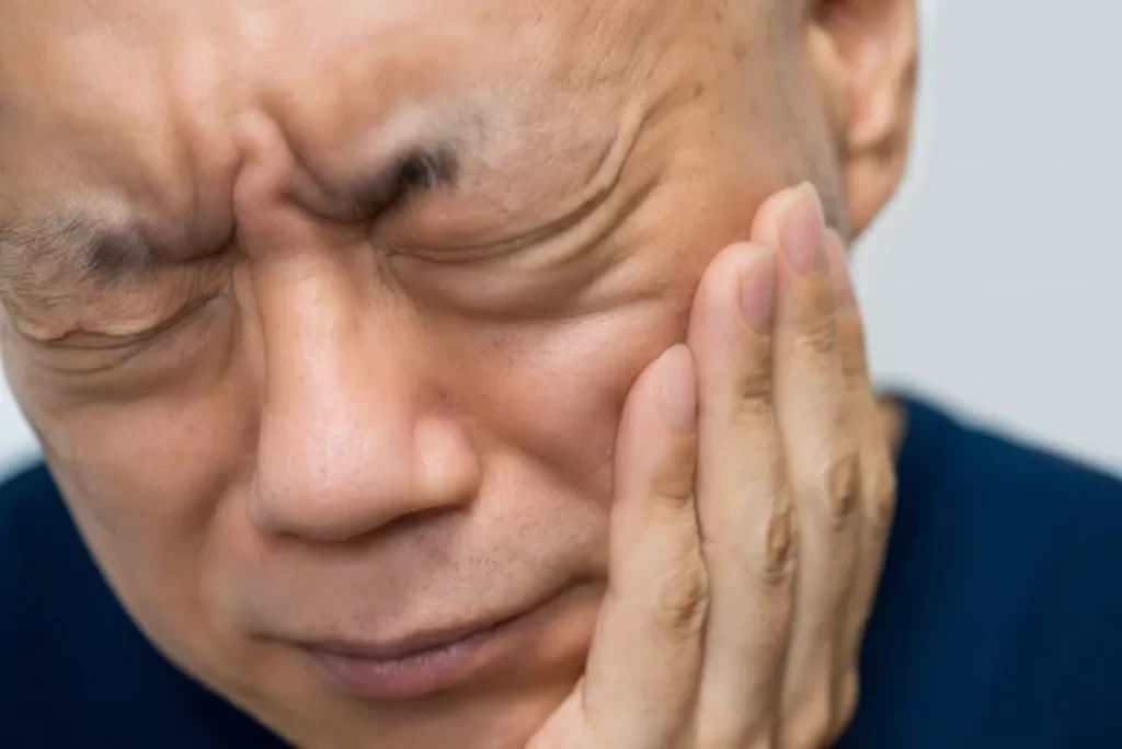 左の歯が痛み、ほっぺを押さえて苦しむ中年男性の顔のクローズアップ