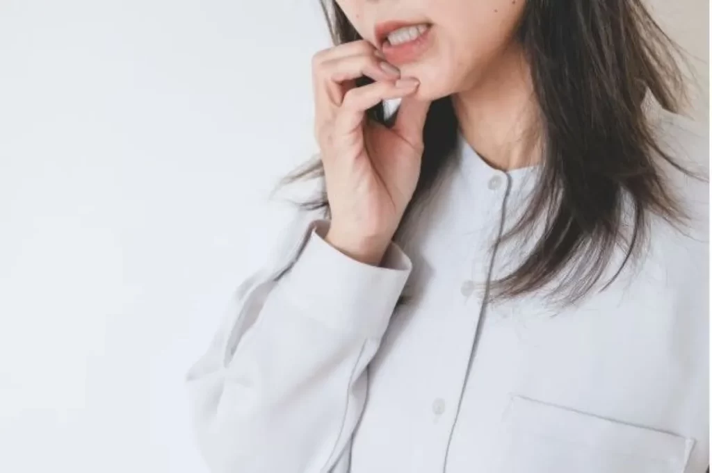 ベージュ色の服を着た女性が歯茎の出血を気にして口を開けている様子