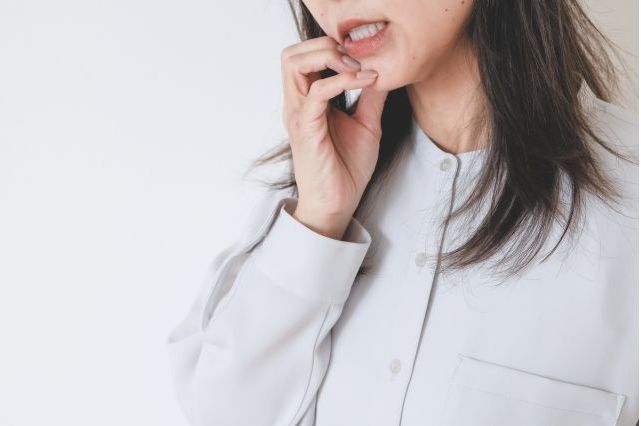 ベージュ色の服を着た女性が歯茎の出血を気にして口を開けている様子