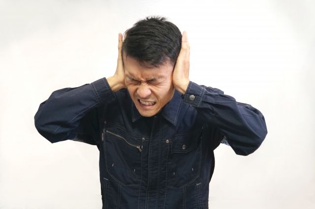 耳の奥の痛みで両耳を押さえる男性