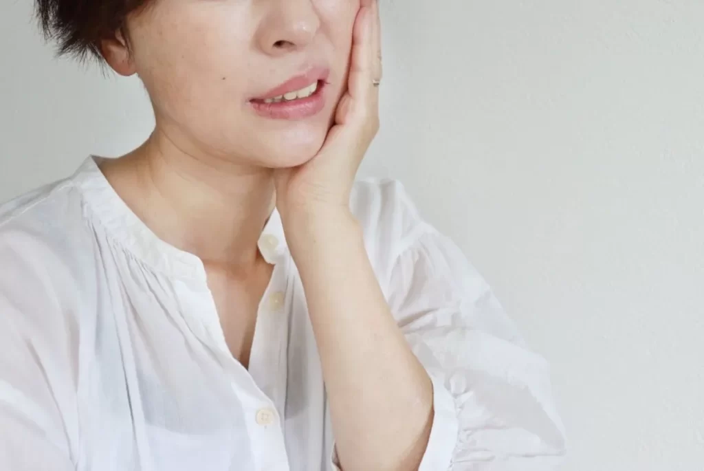 左ほっぺを押さえて顔半分が痛い様子の女性。三叉神経痛や顔の痛みをイメージした写真。
