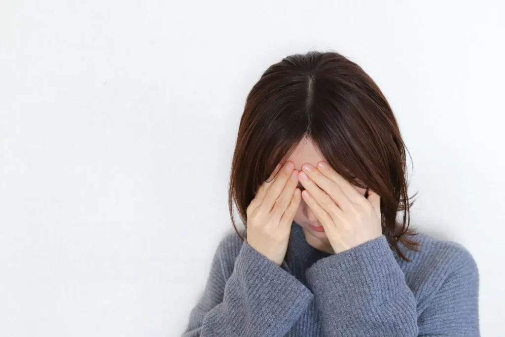 グレーのセーターを着た女性が、強いめまいで頭を下げ、おでこを両手で押さえている様子を表すイメージ写真。