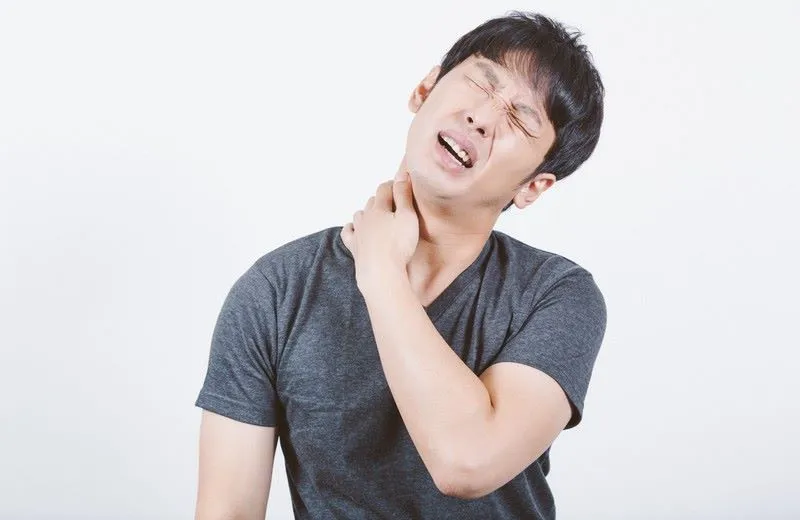 グレーの半袖シャツを着た男性が、左首の横を痛そうに触り、苦悶の表情を浮かべている画像。首のこりと痛みの症状を表すイラスト。