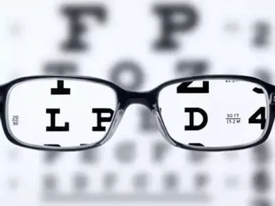 眼鏡をかけた状態で英文字がクリアに視認可能だが、背景の視力検査表の文字がぼやけている近視の症状を示す画像。鍼治療による視力改善の効果を象徴。