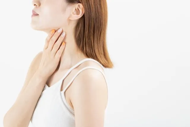 白いキャミソールを着た女性が、喉に違和感を感じて触っている様子。