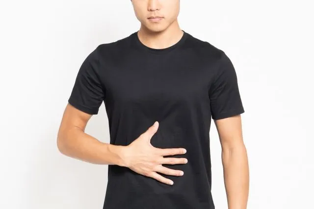 胃痛に苦しむ男性が黒いTシャツ姿で腹部を押さえている様子。十二指腸潰瘍の症状を表すイラストレーション。