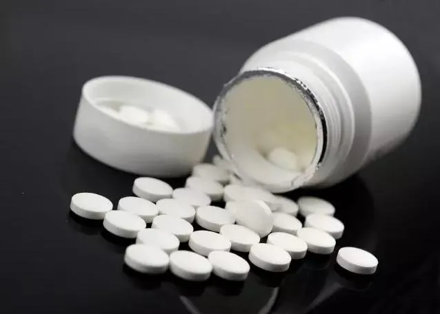 白い薬瓶からテーブルに並べられた白い錠剤のクローズアップ。西洋薬の副作用として冷え性を引き起こすイメージ。