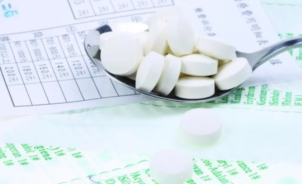 スプーンに盛られた白い精神科薬の錠剤と、処方箋や薬剤費用の紙が複数枚散らばっている画像。向精神薬の多剤服用と副作用の象徴