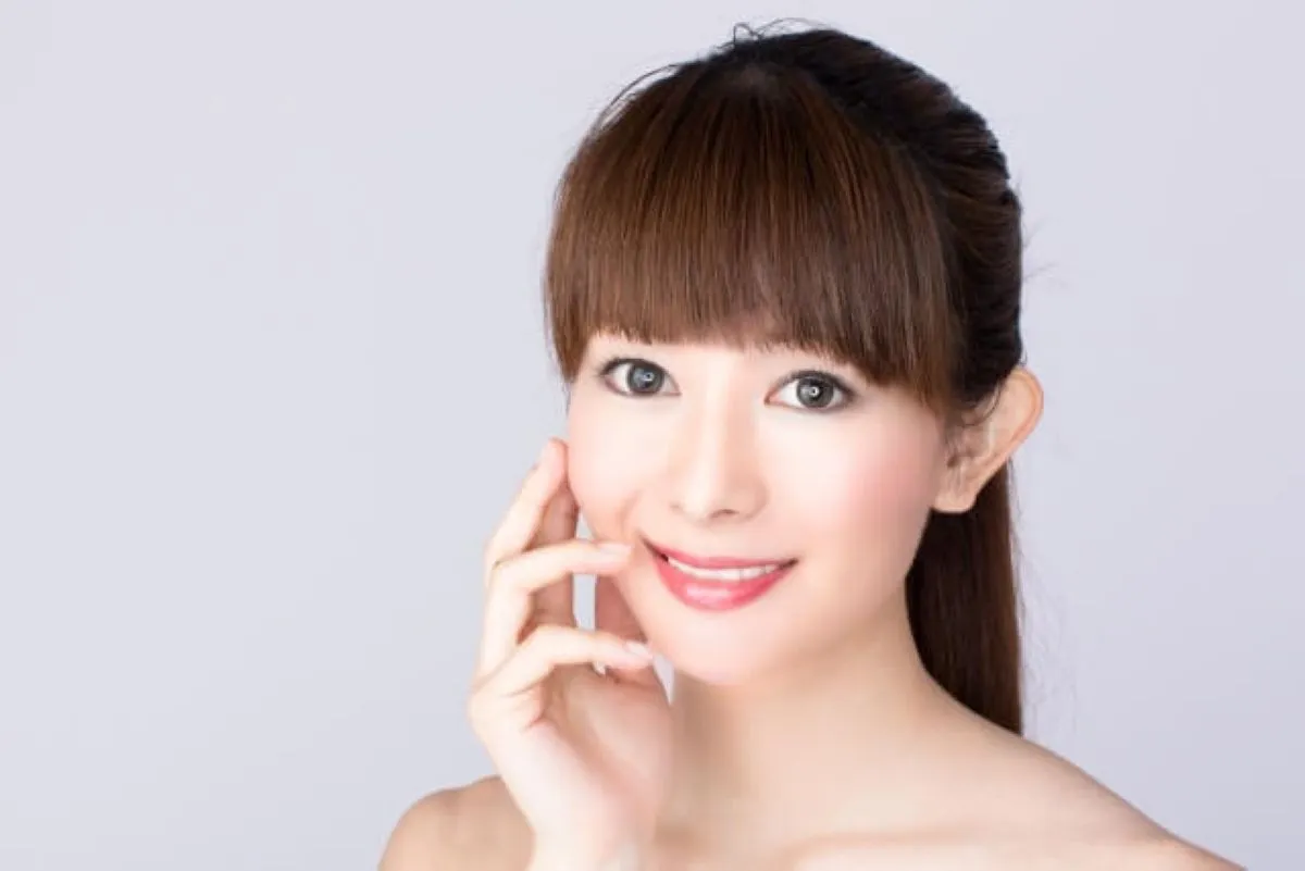 透明感のある美肌の女性が微笑みながらほっぺを優しく触っている様子