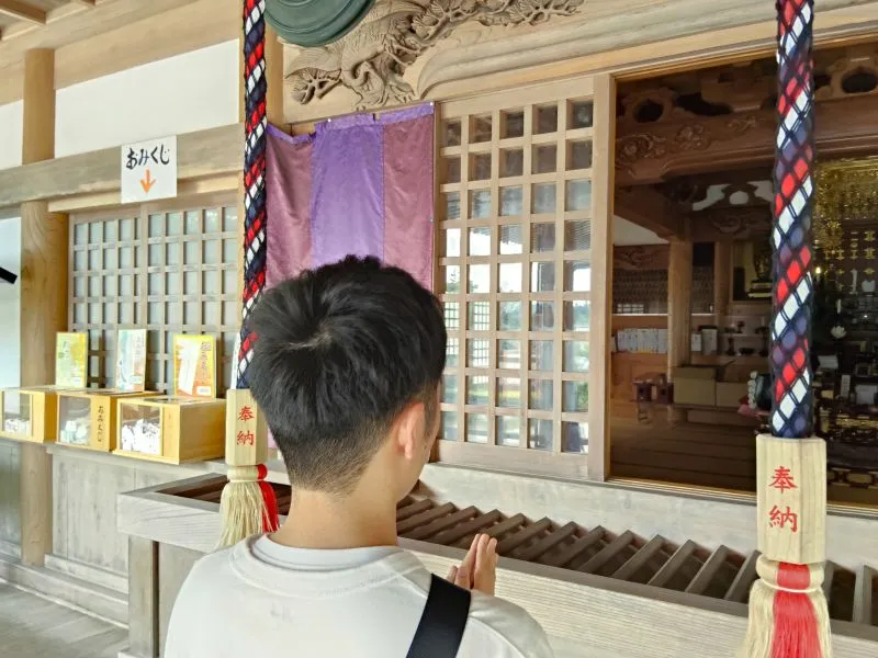 神社で若い男性が背中を向けて合掌し、静かに祈っている様子の写真。