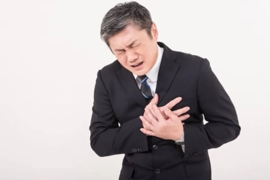 スーツ姿の男性が左胸を両手で押さえ、苦しそうな表情をしている様子