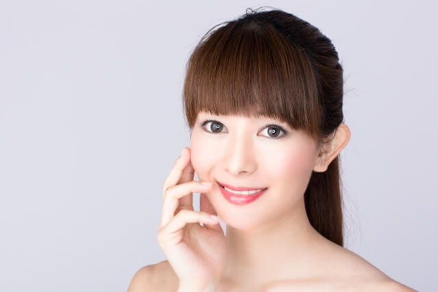 女性が笑顔で顔の肌を触り、美肌をアピールする様子