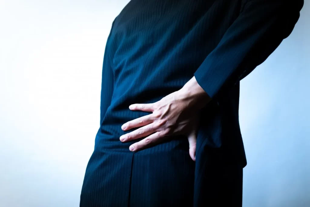 腰痛で苦しむ男性が右手で腰を押さえている背中のクローズアップ画像