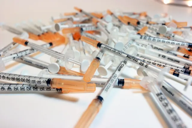 ワクチン注射器が大量に積み重なった様子。ワクチン接種の大量生産を象徴。