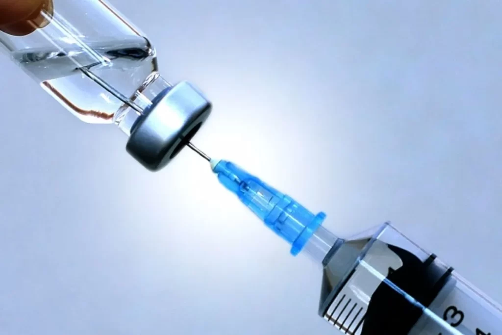 青い注射器が透明なワクチンビアルから液体を吸引するクローズアップ写真。医療・予防接種のイメージ