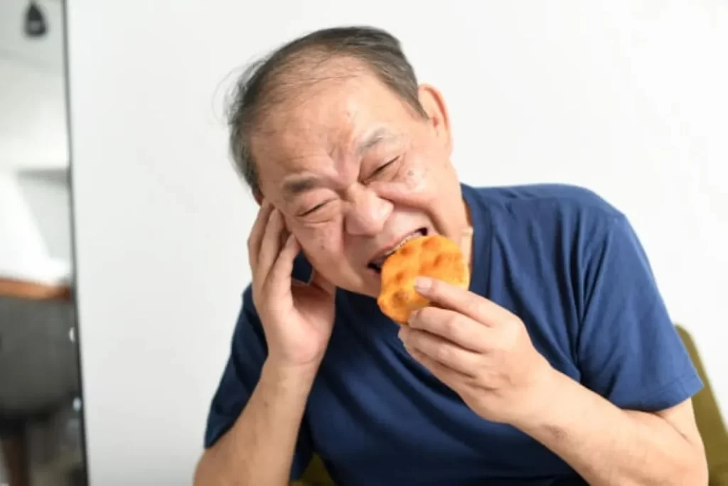 せんべいを食べた際に歯が痛み、右頬を押さえる高齢男性
