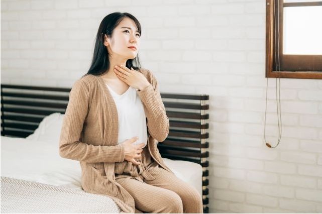 ベッドに座る若い女性が首を触り、甲状腺の腫れを気にしている様子