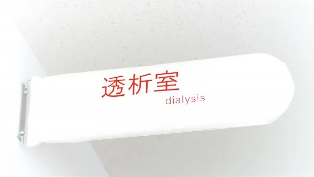 白い看板に赤い文字で「透析室」と書かれた標識のクローズアップ画像。腎不全治療の文脈で人工透析の脅威を象徴。