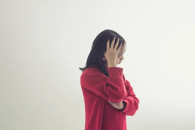 乳がん診断を受けて落ち込む赤いセーターの女性が頭を触る様子