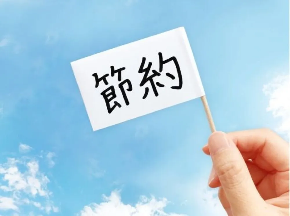 青空を背景に『節約』と書かれた旗を持った手。鍼灸治療中のエネルギー節約を象徴。