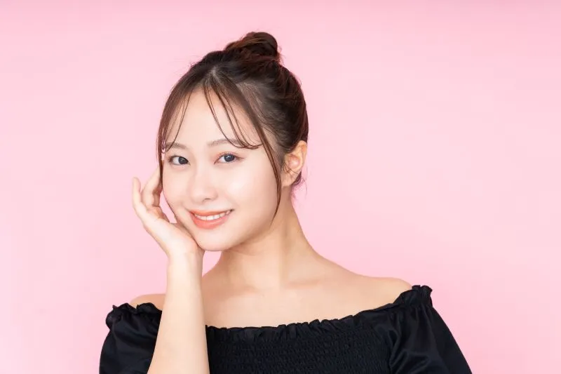 耳を軽く触りながら安心した表情で笑う女性の写真