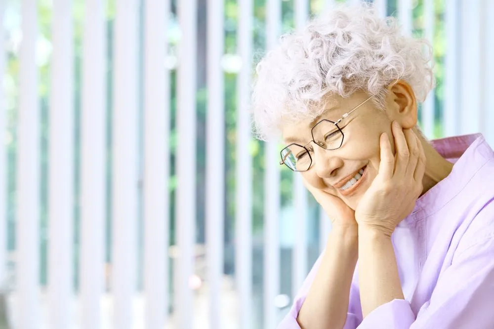白髪のシニア女性が顔面神経麻痺の治療後、顔の歪みが半分以上改善し、笑顔で喜んでいる様子。