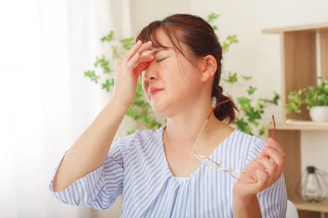 中年女性がメガネを持ち、目の内側を押さえて緑内障による目の不調を訴える様子