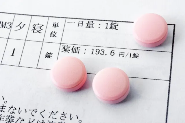 ピンク色の錠剤と薬価が記載された説明書の一部。西洋薬が高純度の化学薬品で副作用が多いことを示すイメージ。