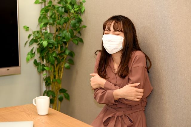 マスクをした女性が寒そうに両腕を撫でている様子