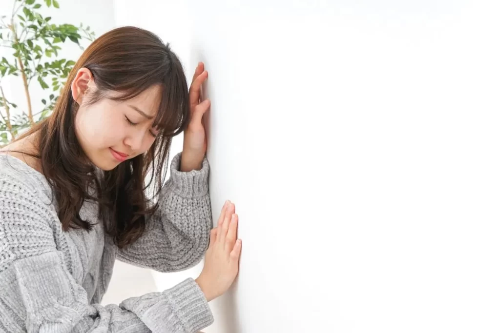 貧血でふらつき、壁に手をついて目を閉じている女性