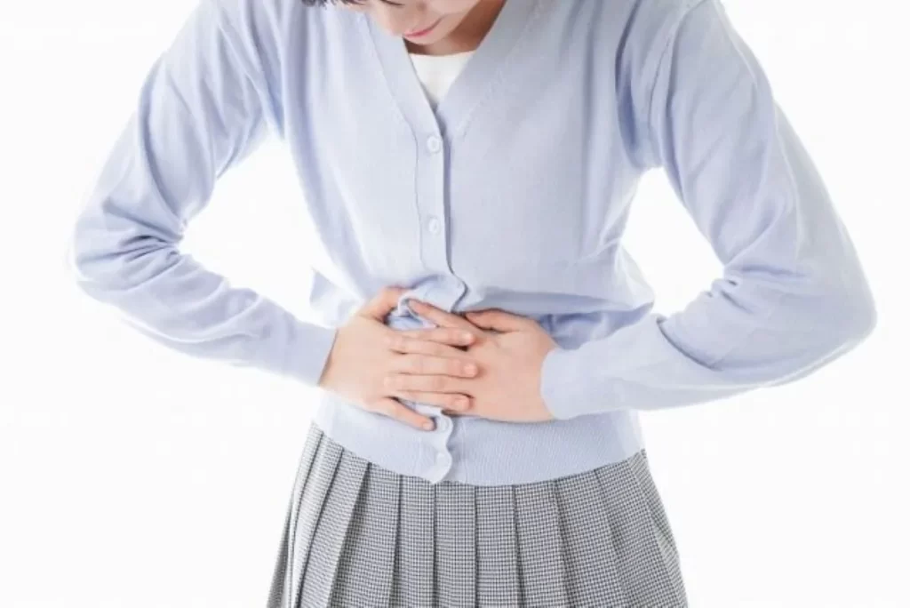 生理痛でお腹を押さえる女性（水色服）