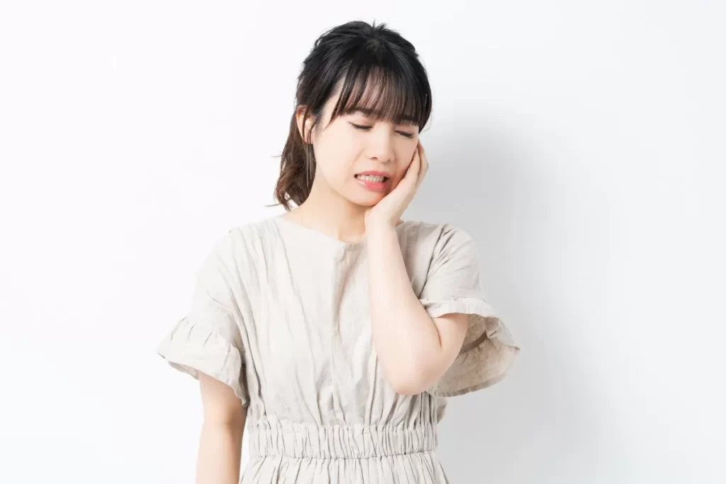 歯根の腫れによる違和感や歯の痛みで頬を押さえる女性