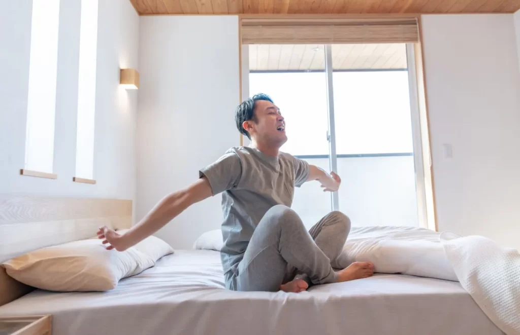 よく眠れて笑顔の男性がベッドに座って両手を広げている写真