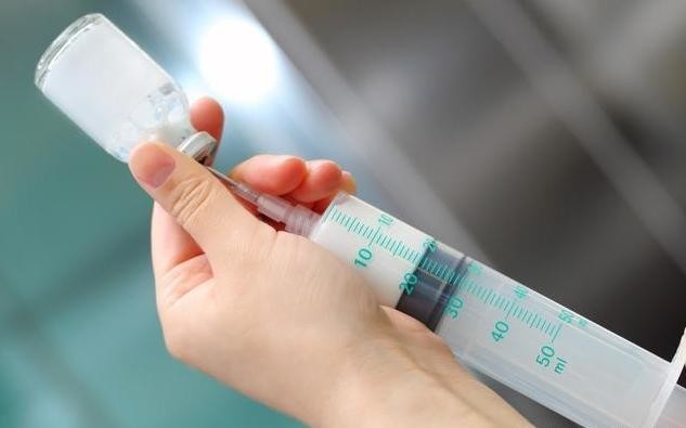 医師の手が注射器で白い薬品を抽出している様子