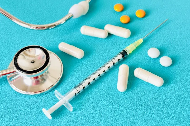 聴診器と注射器、白色とオレンジ色の薬が並んだ医療イメージ