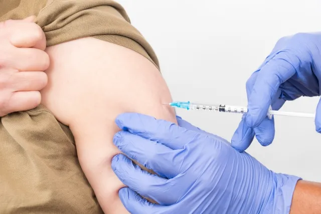 青い手袋の医師が女性の腕にワクチン注射をしている画像。薬害による腎臓障害を暗示