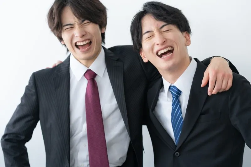 肩を組んで笑う若い男性会社員2人