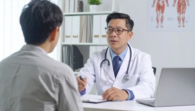 男性医師がデスクに座り、患者の男性に真剣な表情で説明している様子。子宮頸がんの診断結果を伝える場面。
