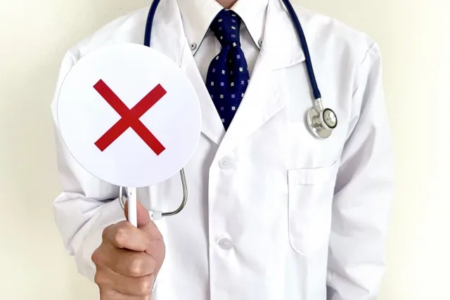 白衣の男性医師が、赤いバツマークのついた白い丸い看板を持っているイラスト。中医学視点からの西洋医学批判を象徴